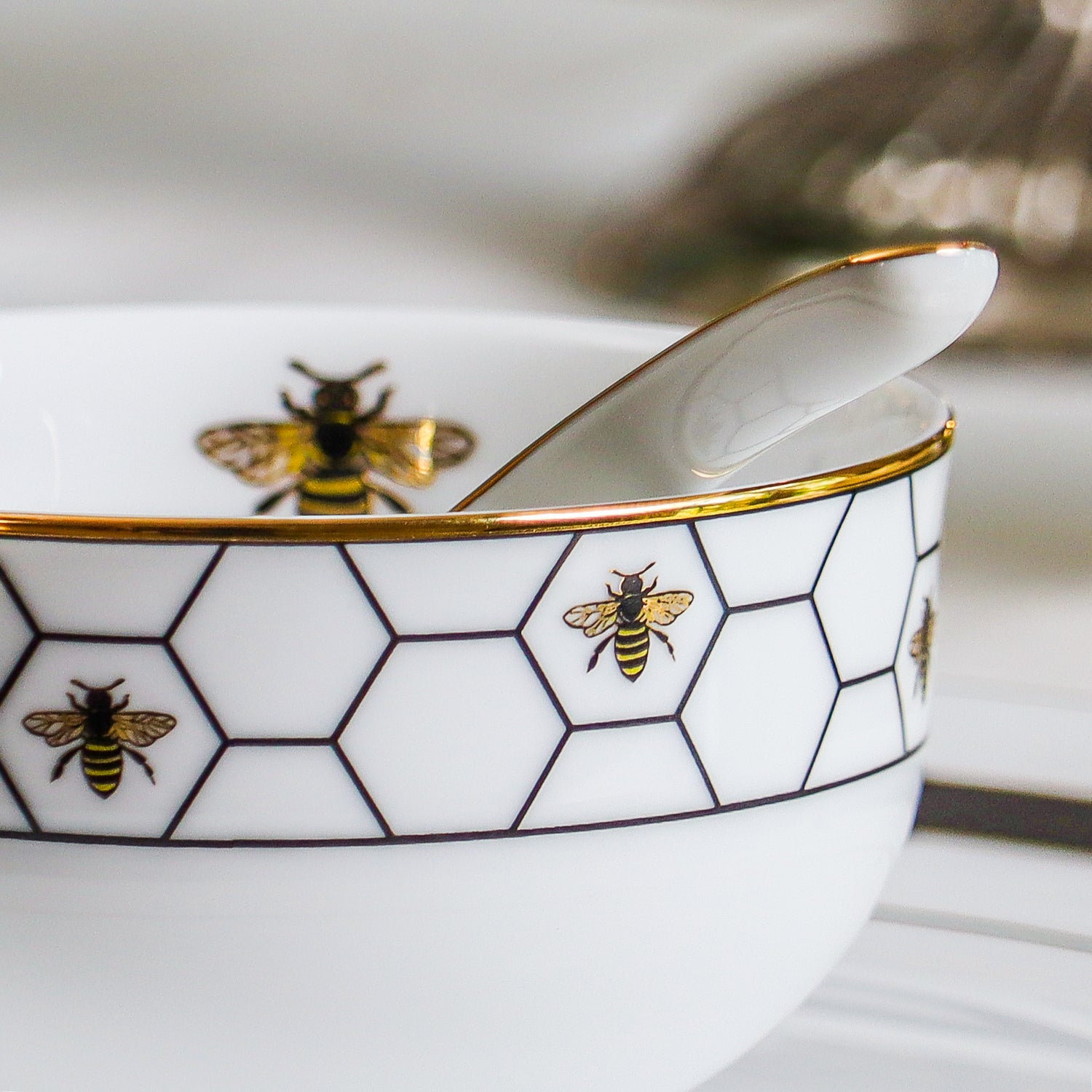 White soup bowl with gold rim and bee pattern on a blurred background
